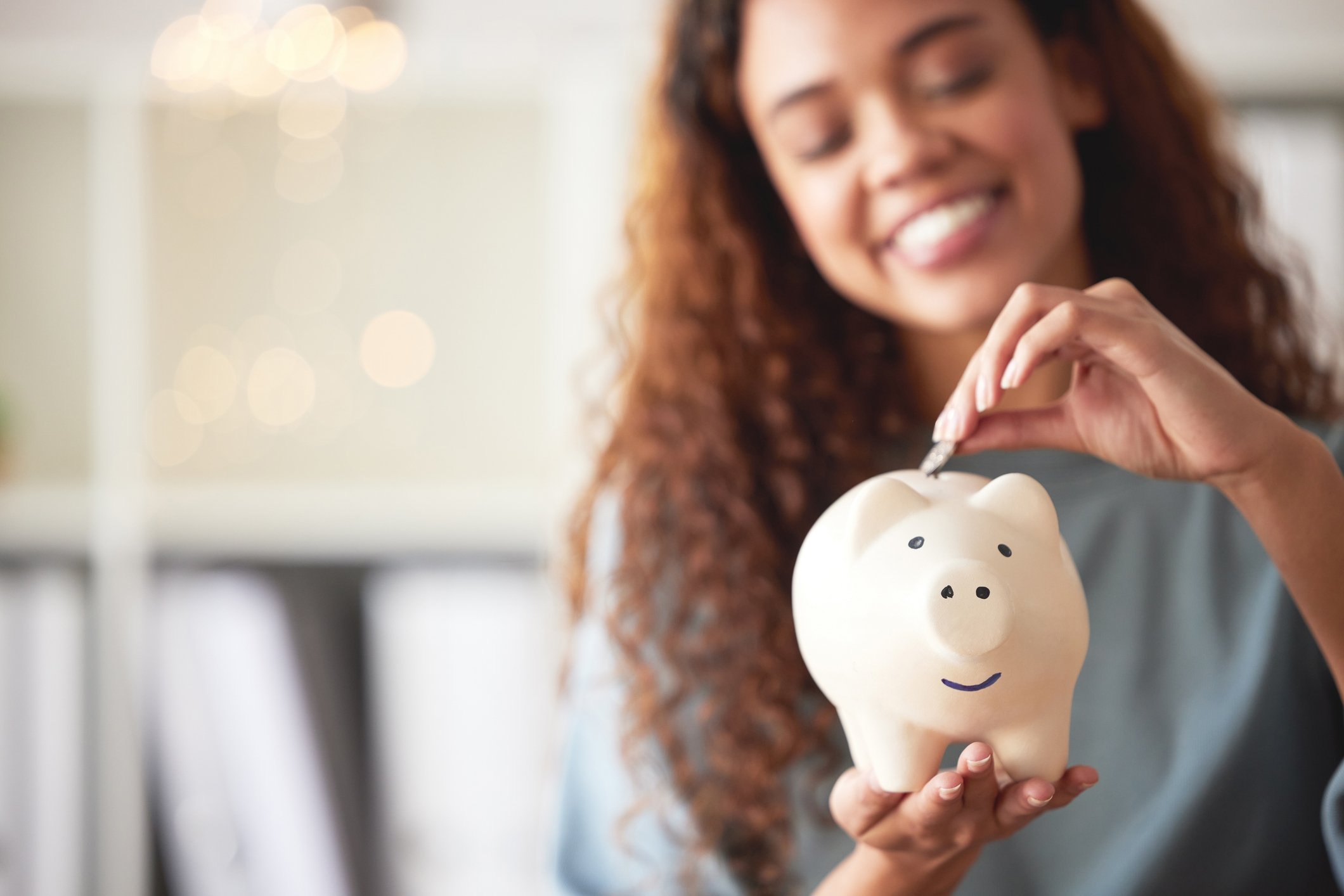 Young woman putting a coin in a white piggy bank