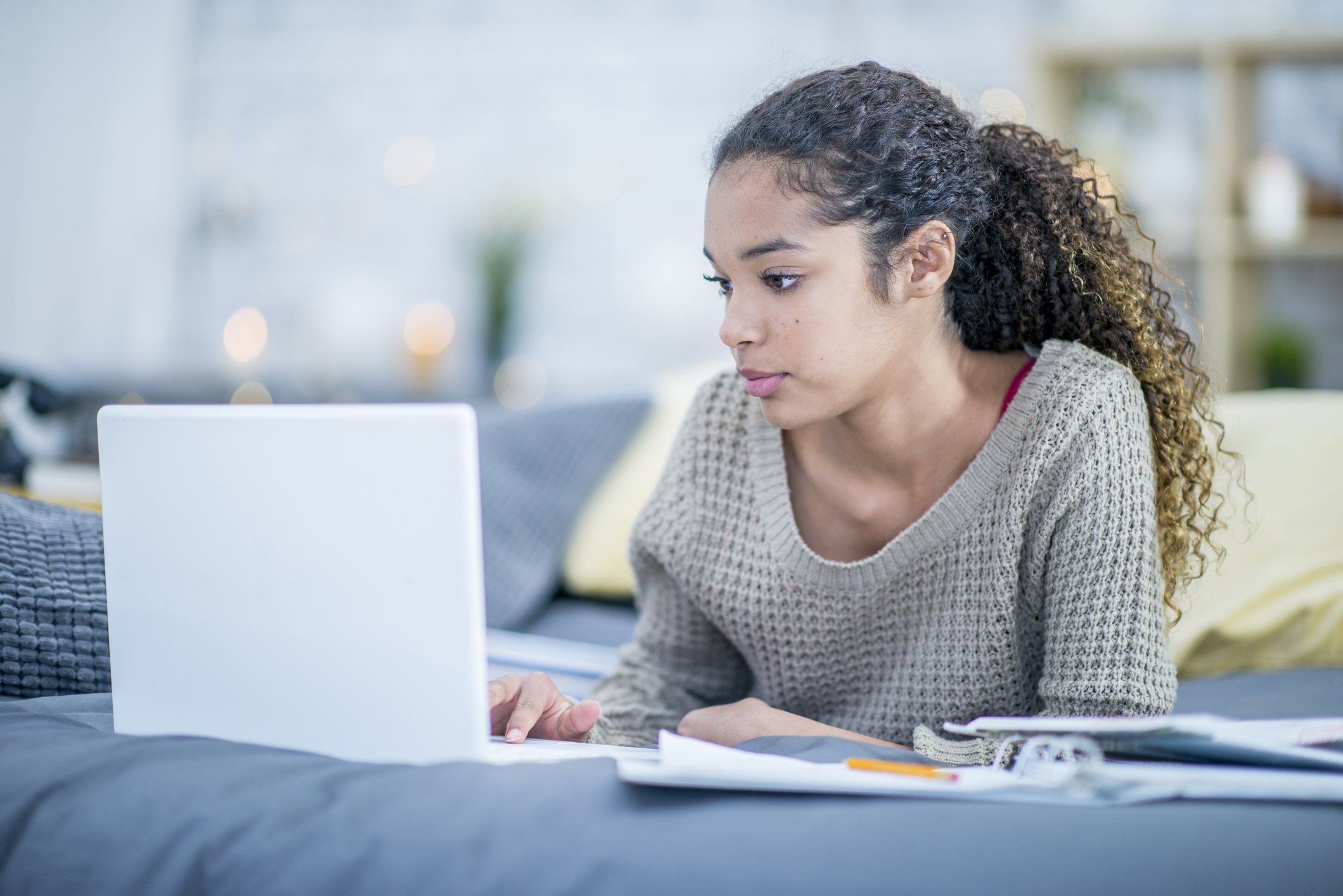 Female teenager studying on her laptop on her bed in her room