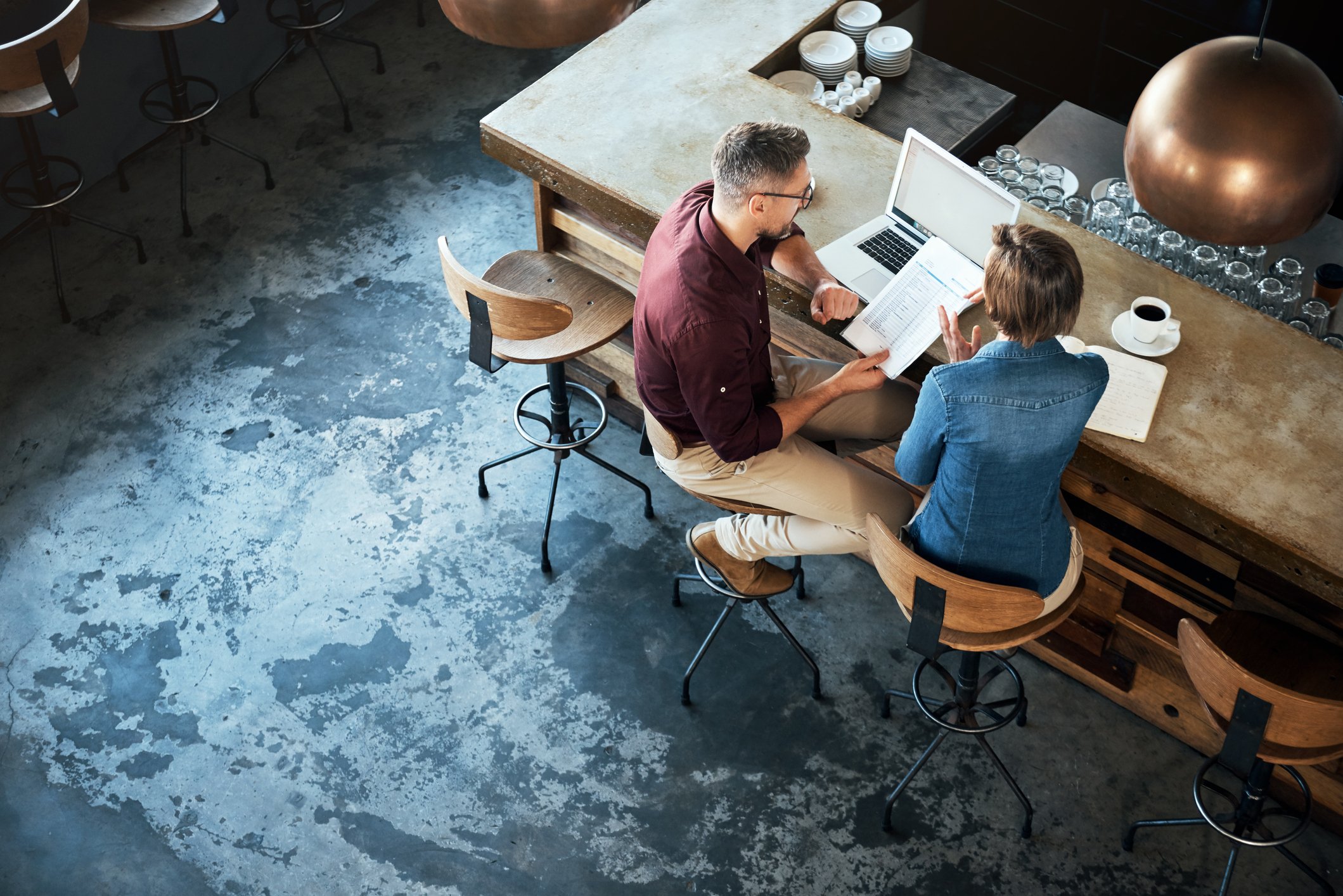 Overhead view of a man and woman sitting at a counter of a restaurant going over papers, bills with their laptop