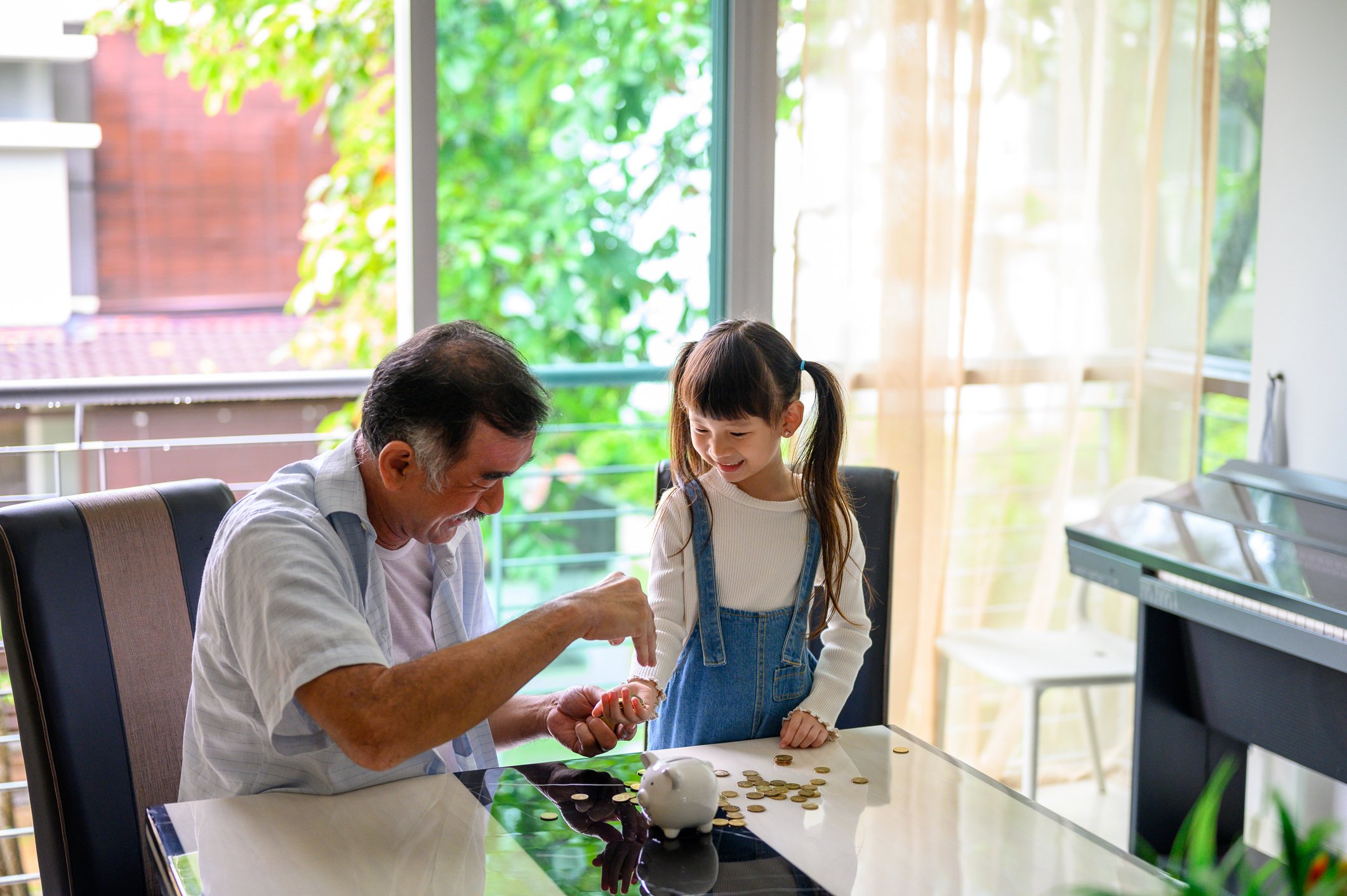 Grandfather counting coins in a piggy bank at the dining table with his granddaughter